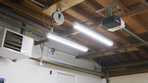 A pair of four foot LED strip lights are shown hanging from a garage with T8 style LED tubes installed.