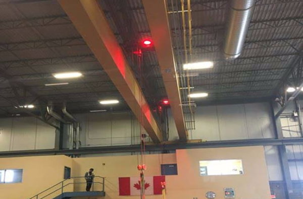 A series of circular red colored LED spotlights are shown mounted high up on an overhead crane used in a Canadian manufacturing facility