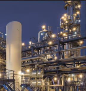 An oil refinery is shown with piping and storage tanks illuminated by explosion proof LED lighting fixtures