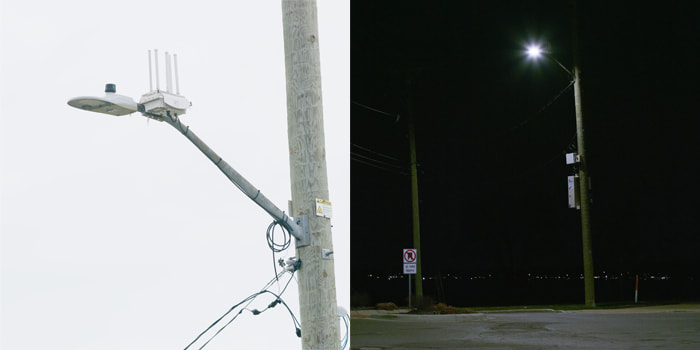 LED street light mounted on top of a parking pole during the day and night projecting illumination onto the roadway below
