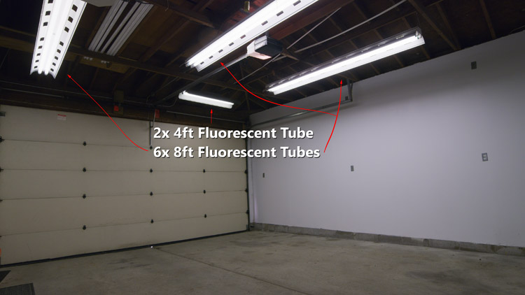 Four lighting fixtures with fluorescent tubes providing dim illumination to a garage workshop area before switching to LED T8 strip fixtures