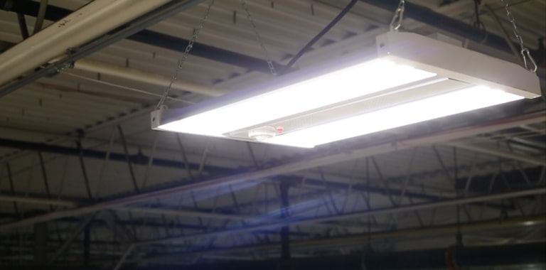 A linear high bay fixture suspended from a warehouse ceiling using four chain hooks illuminates the floor below