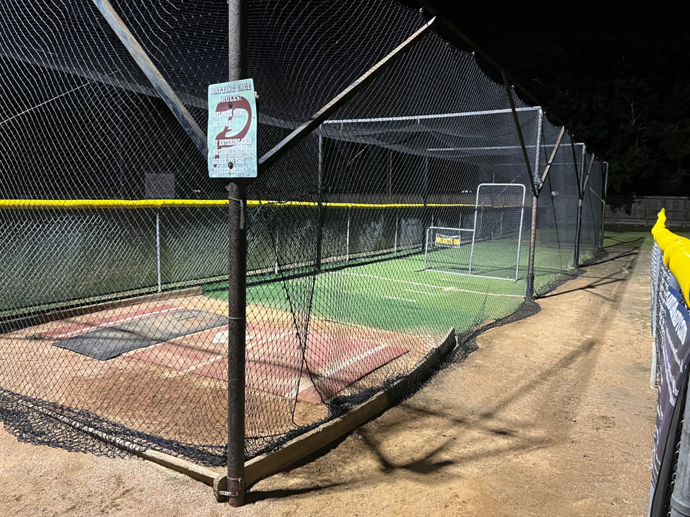 View inside a batting cage with LED flood lights illuminating the area at night.