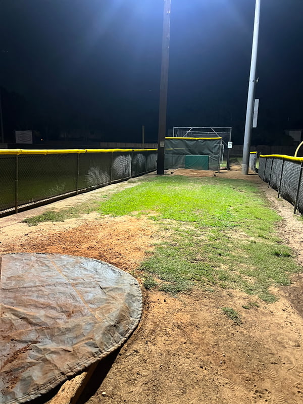 Bright LED lights illuminating the ground inside a pitching cage at night.