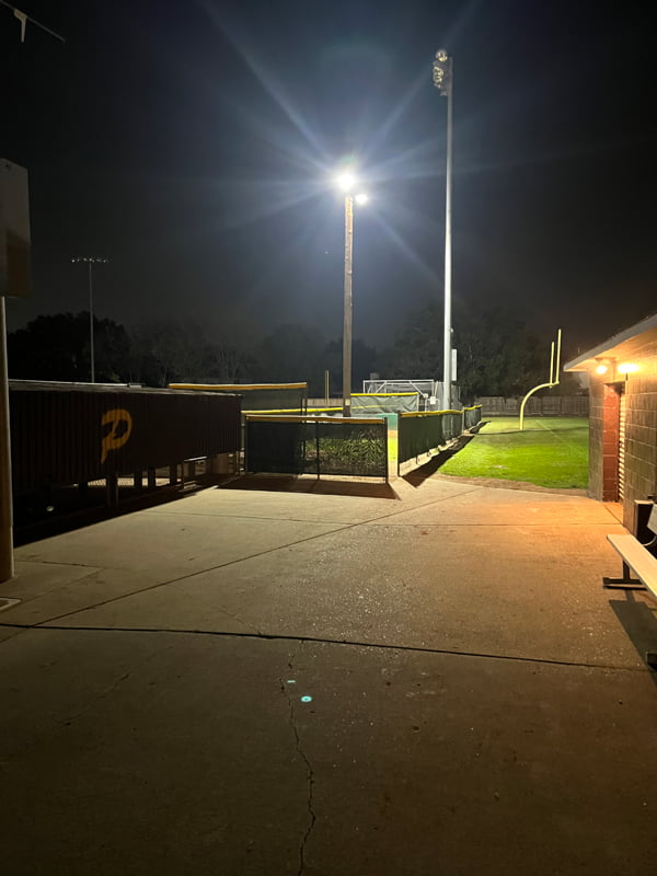 Two LED sports lights mounted on a pole illuminating a pitching cage at night