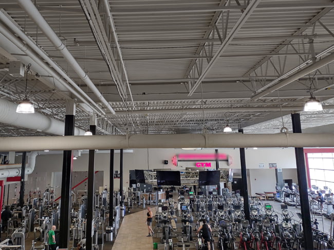 Round shaped high bay fixtures with a reflector illuminating a gym full of weights and exercise equipment