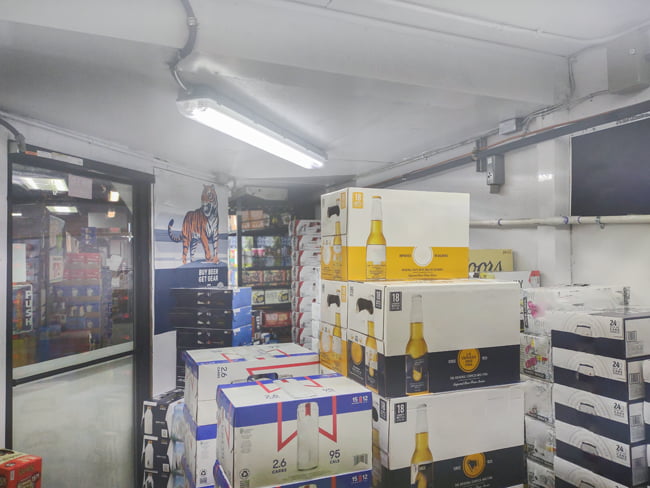 LED vapor tight fixture with LED tubes enclosed in a cold resistant casing mounted on the ceiling of a walk in cooler illuminating cases of beer