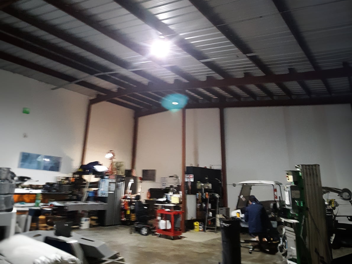 LED UFO High Bay Light illuminating an aircraft hangar with vehicles and forklifts.