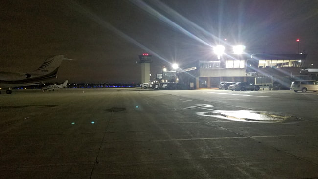 High powered LED flood lights on an airport tower roof illuminating the large parking lot in the surrounding area.