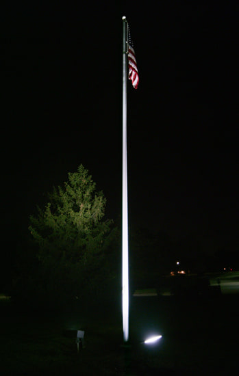 American flag on a pole that's being properly illuminated by two knuckle mount LED flood light fixtures pointed upward