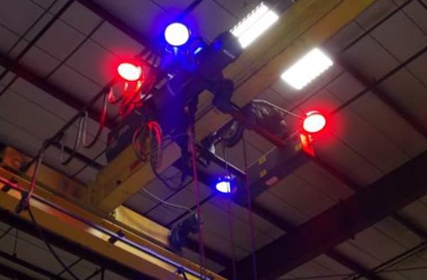 A circular blue colored LED crane light with a spotlight beam pattern is shown mounted high up on a crane in conjunction with red crane lights