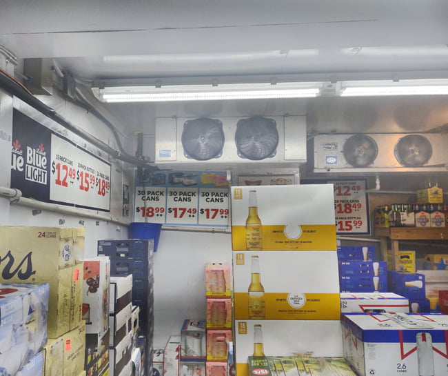 Two LED vapor proof fixtures mounted on the ceiling of a walk in freezer illuminating the cases of beer inside