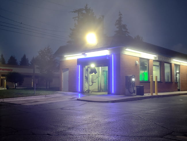 An LED flood light mounted on the rooftop of a small car wash illuminating the entrance and parking lot