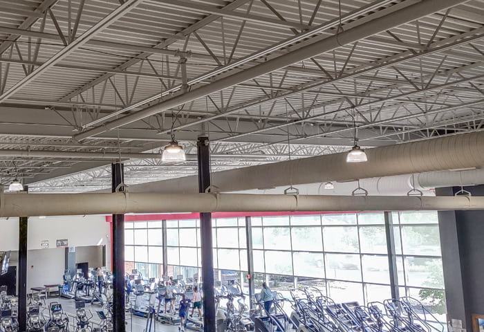 Round shaped LED ufo high bays mounted on a gym ceiling casting illumination around the treadmills below