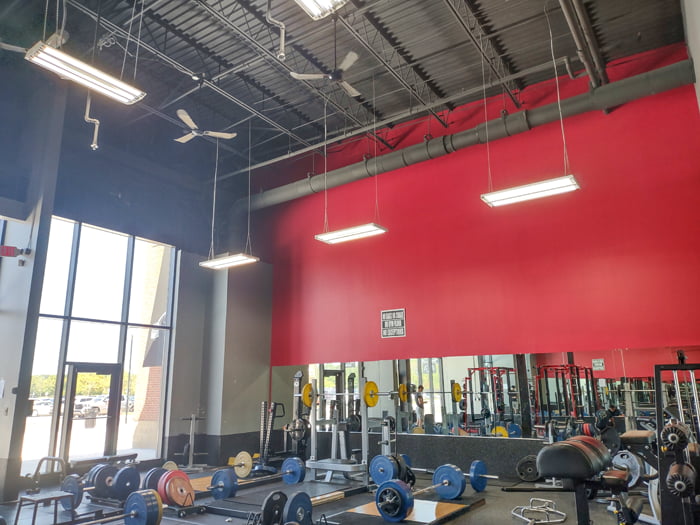 Suspended LED tube ready fixtures hanging from a gym ceiling and casting illumination around the free weight area