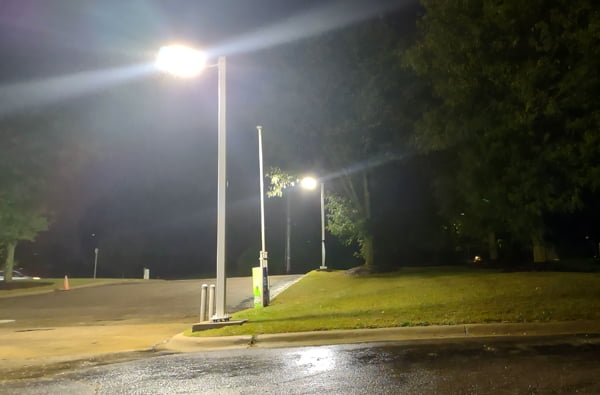 Two LED flood lights mounted with an adjustable slipfitter pole mount casting illumination onto a small commercial parking lot