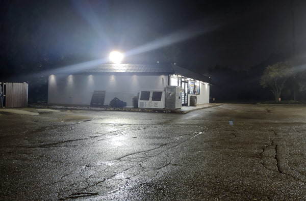 LED flood light mounted on a gas station roof top casting illumination around the building exterior and parking lot