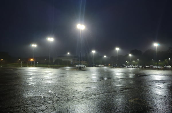 Multiple LED flood lights mounted on parking lot lighting poles casting illumination throughout a school parking lot